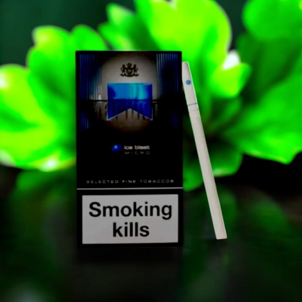 ซองบุหรี่ Marlboro Ice Blast วางบนโต๊ะไม้ในบรรยากาศป่าเขียวขจี แสดงดีไซน์ซองสีดำแถบฟ้าที่เป็นเอกลักษณ์