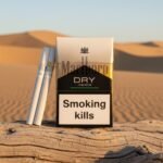 ซองบุหรี่ Marlboro Dry Menthol และมวนบุหรี่ วางบนขอนไม้ท่ามกลางทิวทัศน์ทะเลทรายสีทอง