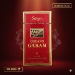ซองบุหรี่ Gudang Garam 12 สีแดงขอบทองสุดคลาสสิก วางบนพื้นหลังสีแดงเข้มไล่เฉด มีกราฟิกควันพริ้วไหวรอบซอง พร้อมข้อความ Authentic Kretek และ Rich Aroma