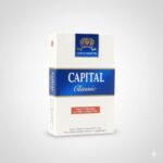 บุหรี่ Capital Double Apple ซองสีเขียวสดใสรูปแอปเปิ้ลคู่ พร้อมมวนบุหรี่วางบนโต๊ะไม้ในบรรยากาศป่า